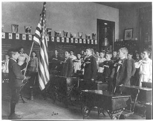 In 1899, school children pledge to the flag, using  original hand gestures