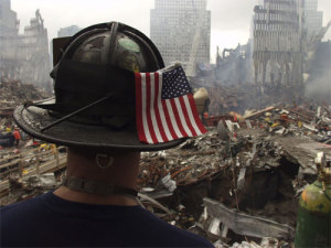 A fireman stands amid rubble with a 911 flag on his helmet