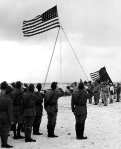 Japanese soldiers salute the American flag after surrendering Wake Island