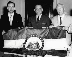 Three men, including her son (right), show off Marie Oliver's original hand-sewn silk Missouri state flag. (State Historical Society)