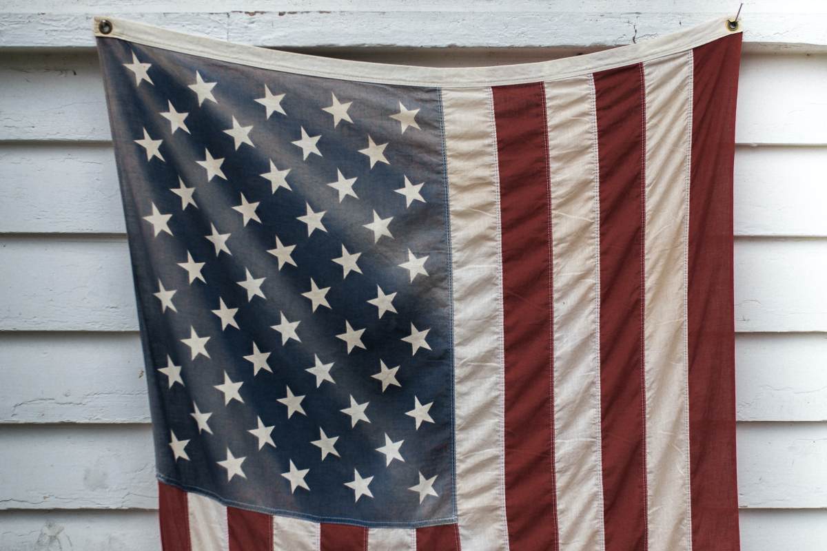 american flag hanging against a white sided house