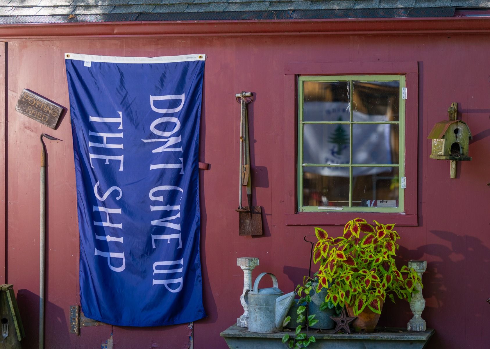 Commodore Perry Don't Give Up the Ship flag hung vertically on a red shed wall as outdoor decor
